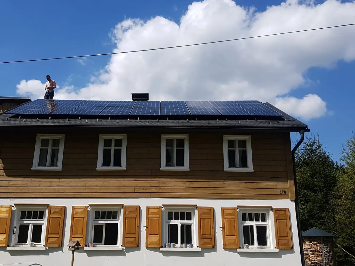 Roubený dům s fotovoltaikou, technik na střeše