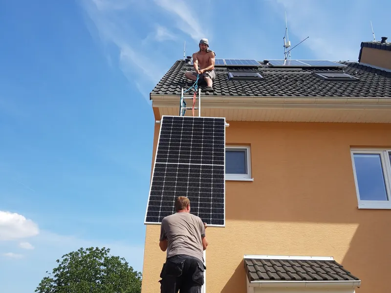 Technici vynášejí panel po žebříku na střechu